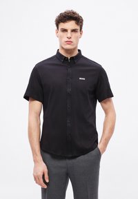 Μαύρο κοντομάνικο πουκάμισο με γιακά με κουμπιά, διαθέτει μικρό λευκό λογότυπο "BOSS" στο αριστερό μέρος του στήθους και λείο βαμβακερό ύφασμα.