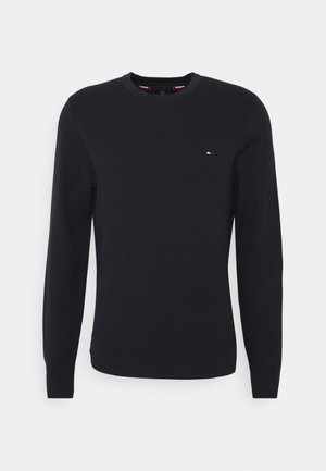 Schwarzer Pullover mit langen Ärmeln und Rundhalsausschnitt, mit kleinem rot-weiß-blauem rechteckigem Logo auf der linken Brust.