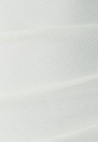 Texturovaná bílá tkanina s měkkým, vlnitým vzorem, obsahující jemné variace v odstínech a hladkým, uvolněným padáním.