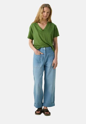 Green v-neck t-shirt, relaxed fit; light blue wide-leg jeans with two front pockets; model wearing black sandals; smooth fabric textures.