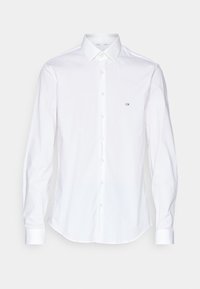 Vit långärmad skjorta med knappstängning, spetsig krage och liten "CK"-logotyp broderad på vänstra bröstet.