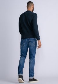 Sudadera azul marino con puños acanalados, combinada con jeans de un azul claro. Los jeans tienen un diseño de bolsillo trasero y están ligeramente enrollados en los puños.