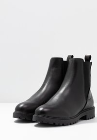 Para czarnych skórzanych butów Chelsea z elastycznymi panelami bocznymi i wytrzymałą podeszwą na jasnoszarym tle.