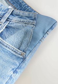 Spijkerbroek met lichtblauwe wassing, voorzien van een contrasterende elastische tailleband, metalen knopen en gedetailleerd stiksel langs de naden.