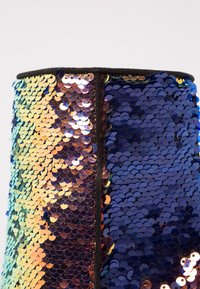 Gros plan d'un panneau de tissu séparé par une couture noire, recouvert de sequins réversibles passant du doré-jaune à des nuances de bleu profond.