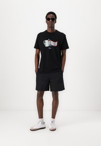 Zwart graphic T-shirt met kleurrijke opdruk, zwarte shorts, witte sneakers met grijze accenten en een zonnebril. Eenvoudig ontwerp met strakke lijnen.