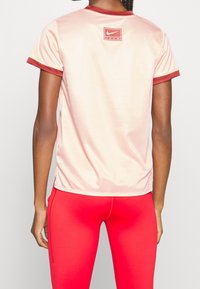 Person som bär en ljus rosa Nike Team t-shirt med vinröd kant och klara röda leggings, sedd bakifrån.