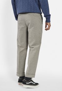 Gray, tailored pants with rolled cuffs, made of a textured fabric. Paired with black Vans sneakers and a blue cable-knit sweater.