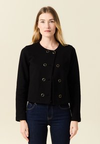 Zwart cropped jack met een ronde halslijn en lange mouwen, voorzien van goudkleurige knopen en een gestructureerde stof. Draag het over donkere jeans.