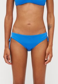 Kék bikini alsó, sima, rugalmas anyagból készült. Oldalsó megkötőkkel és alacsony szabású kivágással. Nincsenek látható minták vagy díszítések. Egyszínű az egész.
