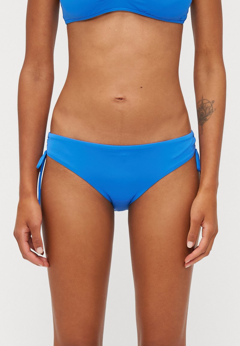 Kék bikini alsó, sima, rugalmas anyagból készült. Oldalsó megkötőkkel és alacsony szabású kivágással. Nincsenek látható minták vagy díszítések. Egyszínű az egész.