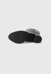 Bottine en cuir noir avec une semelle en caoutchouc texturée et un design minimal, présentant un bout arrondi et un zip sur le côté.