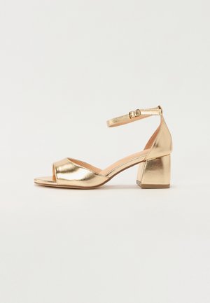 Guldmetal åben-toe sandal med ankelrem og lav blokhæl på neutral baggrund.