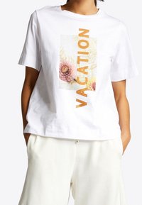 Witte katoenen T-shirt met een bloem- en tekstafbeelding "VACATION" in het oranje op de voorkant. Ontspannen pasvorm met korte mouwen. Ideaal voor casual draag.
