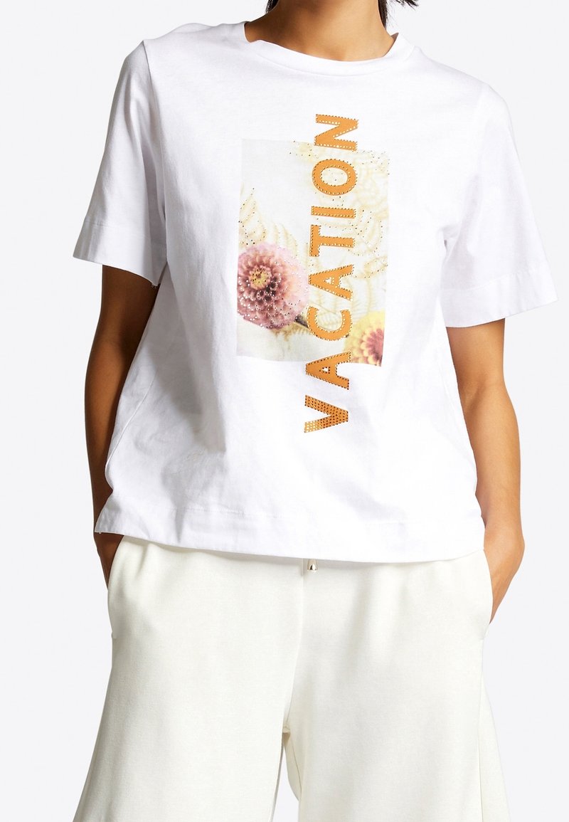 Witte katoenen T-shirt met een bloem- en tekstafbeelding "VACATION" in het oranje op de voorkant. Ontspannen pasvorm met korte mouwen. Ideaal voor casual draag.