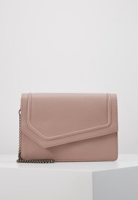 Borsa a mano in morbido cuoio rosa con pattella angolare e tracolla in metallo scuro, appoggiata su una superficie bianca contro uno sfondo semplice.