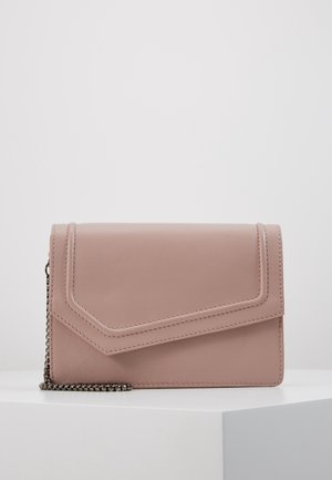 Borsa a mano in morbido cuoio rosa con pattella angolare e tracolla in metallo scuro, appoggiata su una superficie bianca contro uno sfondo semplice.