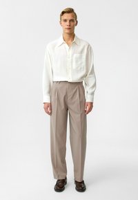 Witte blouse met lange mouwen en een borstzak, gecombineerd met lichtbeige high-waisted broeken en donkerbruine schoenen. Eenvoudig, op maat gemaakt ontwerp.