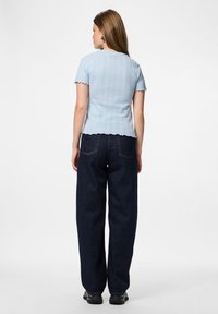 Απαλό μπλε κοντομάνικο πουλοβεράκι με ριγωτή υφή και σκαλιστές άκρες, συνδυασμένο με σκούρους μπλε παντελόνες φαρδιές.