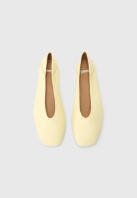 Pantofi comozi galbeni cu vârf rotund și deschidere laterală. Textură netedă cu un design minimal. Căptușeala interioară este maro. Numele mărcii este vizibil în interior.