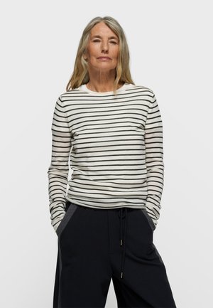 Camicia a maniche lunghe color crema con righe orizzontali nere. Tessuto leggero e morbido. Abbinata a pantaloni neri con coulisse e dettagli laterali.