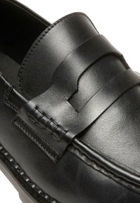 Il mocassino in pelle nera presenta una superficie liscia, una fascia larga sul collo del piede e cuciture dettagliate lungo la suola.