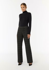 Zwarte turtleneck top in combinatie met zwart-witte geruite broeken met wijde pijpen. Gladde textuur met een aansluitende silhouet en splitdetails aan de zoom.