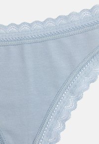 Lichtblauwe katoen string met een geschulpte kantafwerking aan de tailleband, met decoratieve stiksels langs de randen. Zachte en gladde textuur.