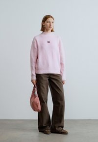 Pulover roz tricotat cu finisaj texturat. Pantaloni maro cu croială largă. Geantă roz deschis și pantofi cu imprimeu animal. Design minimalist.