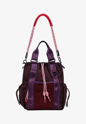 Lila Stofftasche mit einem Netzfach, roten Akzenten und rosa-weiß gestreiften Griffen. Verfügt über einen gerafften oberen Bereich mit Kordelverschluss.