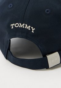 Tengerészkék baseball sapka, hátul hímzett "TOMMY" felirattal, fémből készült állító csattal és texturált anyaggal.