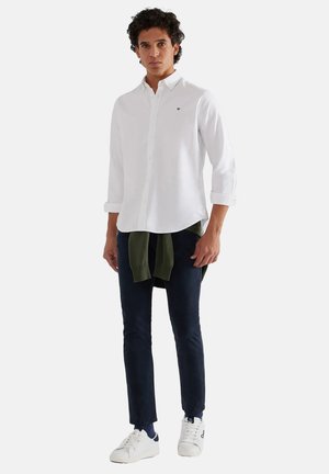 Camisa blanca de botones con mangas remangadas, pantalones navy, suéter verde atado a la cintura y zapatillas blancas con acentos navy.