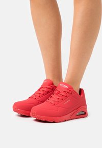 Czerwone buty sportowe o gładkim, matowym wykończeniu, z panelami z siateczki dla lepszej wentylacji oraz amortyzowaną podeszwą z widoczną jednostką powietrzną.