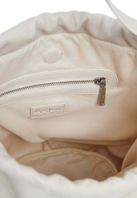 Interior de un bolso de mano de cuero color beige con un bolsillo con cremallera. Forro de tela suave y una etiqueta con el nombre de la marca. Diseño de parte superior redondeada y fruncida.