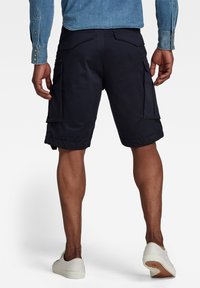 Navy cargo shorts made of breathable fabric with side pockets, cuffed hem, and a smooth texture, paired with white shoes.