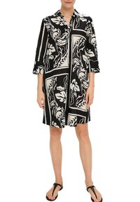 Robe à motifs floraux noir et blanc avec des manches trois-quarts, col, fermeture à boutons et coupe droite. Tissu léger avec des sections contrastantes.