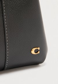 Fekete bőr kézitáska kavicsos hatású textúrával, arany színű fémhardverrel, varrott díszítéssel és feltűnő logóval az oldalon.