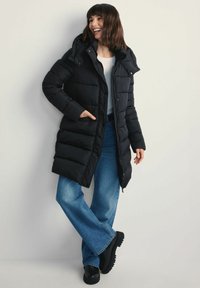 Czarna kurtka puchowa z kapturem, z pikowanym wykończeniem, z przodu na zamek błyskawiczny i zatrzaskami. Połączona z jasnoniebieskimi spódnicami dzwonowymi i czarnym obuwiem.