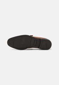 Brauner Lederschuh mit einer glatten Oberfläche und schwarzer Gummisohle mit strukturiertem Muster. Mit Nahtdetails entlang der Kanten.