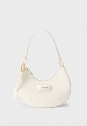 Λευκή τσάντα ώμου σε σχήμα ημισελήνου με εξαρτήματα σε χρυσή απόχρωση, κλείσιμο με φερμουάρ και λογότυπο "LACOSTE" στην μπροστινή πλευρά.
