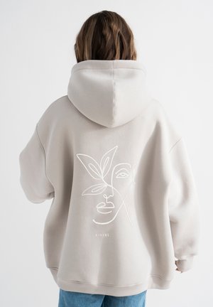 Beige hoodie met een groot geborduurd gezicht en bladdesign op de achterkant. Gemaakt van zachte stof, met een ruime capuchon en geribbelde manchetten.