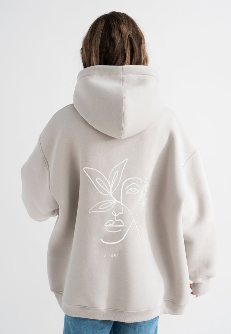 Beige hoodie met een groot geborduurd gezicht en bladdesign op de achterkant. Gemaakt van zachte stof, met een ruime capuchon en geribbelde manchetten.