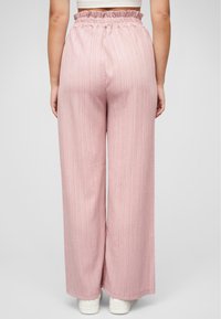 Pantalon large rose clair avec un tissu texturé et une taille élastique froncée, associé à des chaussures blanches.