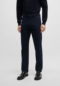 Navy katoenen broeken met een rechte pasvorm, voorzien van een knoopsluiting en riemlussen. Gecombineerd met gepolijste zwarte schoenen.