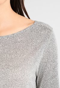 Gray top featuring a speckled black pattern, boat neckline, and smooth texture. Focus on fabric pattern and shoulder detail.