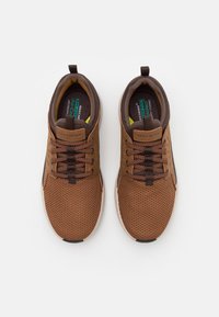 Chaussures de sport en mesh marron avec des accents marron foncé, bout légèrement arrondi, tige texturée et fermeture à lacets. Comprend une semelle intérieure rembourrée et une semelle extérieure en caoutchouc.