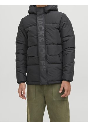 Personne portant une doudoune noire avec capuche et poches à rabat, associée à un pantalon cargo vert sur un fond clair uni.