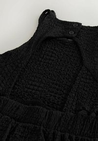 Robe noire texturée avec un design smocké, dotée d'un décolleté rond, d'accents à boutons et de bretelles larges. Volants horizontaux le long de l'ourlet.