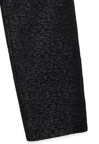 Zwarte leggings met een gepatineerde afwerking, voorzien van een onregelmatig, gemarmerd zwart ontwerp tegen een gladde achtergrond.