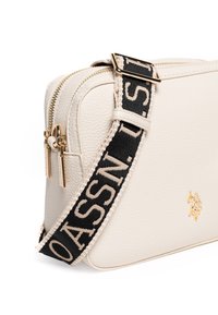 Borsa a tracolla bianca in pelle con finitura testurizzata, hardware dorato, doppie cerniere e tracolla nera a motivo con scritte beige.